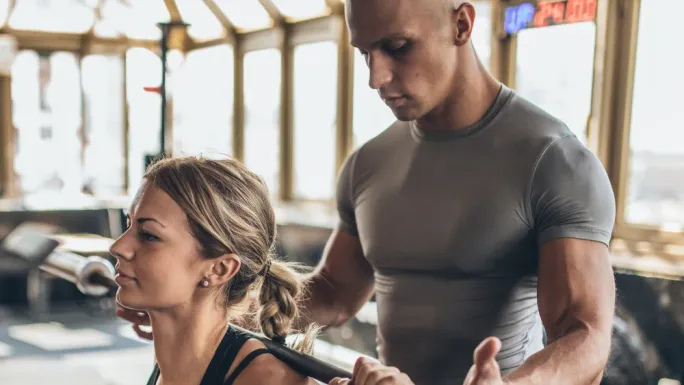 Trainer coaching a client through a guided barbell exercise