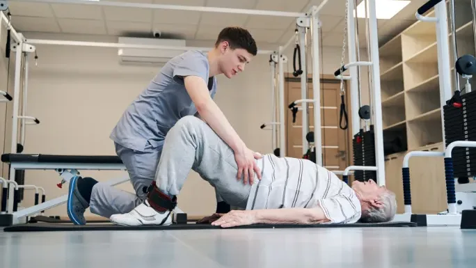 Physical therapist guiding an older patient through a therapeutic hip and back stretch