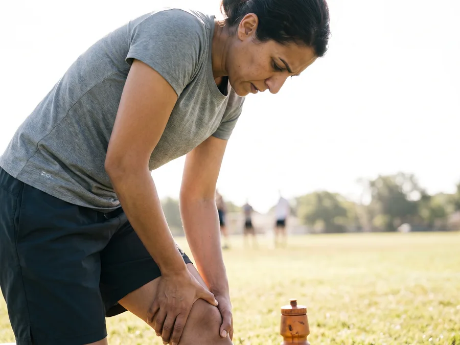 Athlete gripping a painful knee outdoors during training